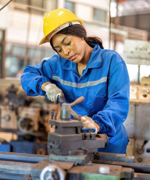 Woman worker in uniform operating machine at factory concentrate on fabrication job on lathe